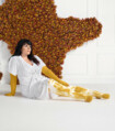 Une femme est assise devant un mur de fleurs. Elle porte un soin de compression jaune avec un motif Batik blanc