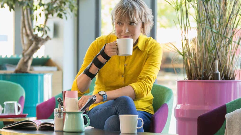 En kvinde bærer en JuzoPro Manu Xtec håndledsbandage og holder en kop i hånden En kvinde bærer en JuzoPro Manu Xtec håndledsbandage og holder en kop i hånden