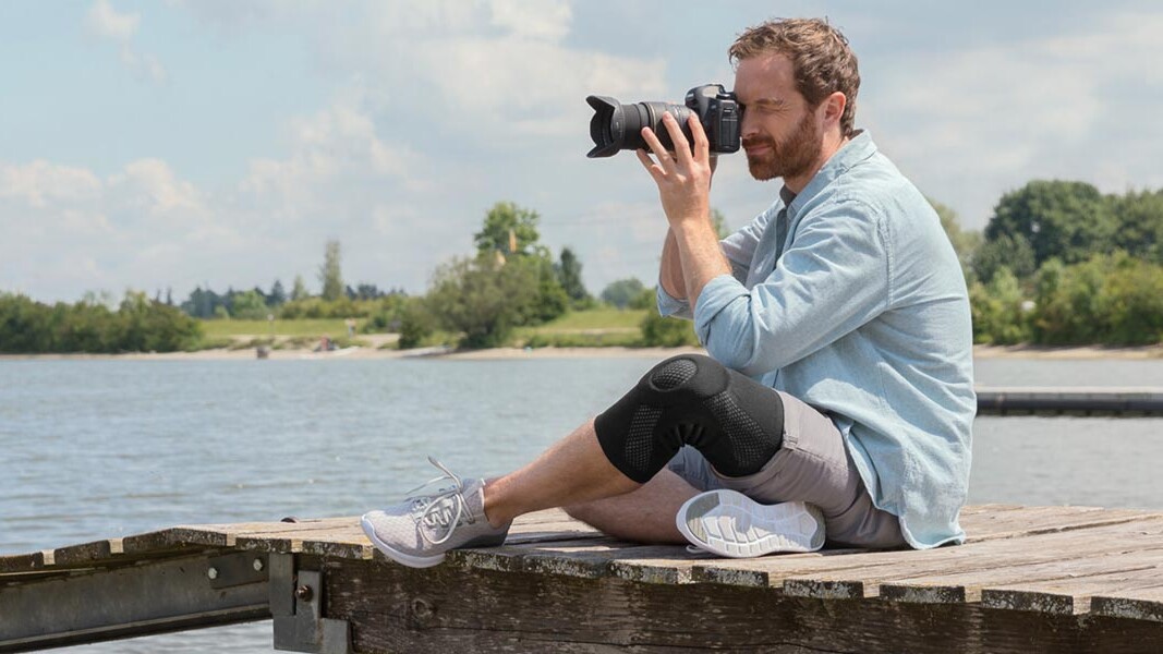 Un photographe est assis sur une passerelle. Il porte une genouillère Juzo.