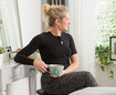 Kvinde med sort thoraxbandage sidder ved et sminkebord og holder en kop te