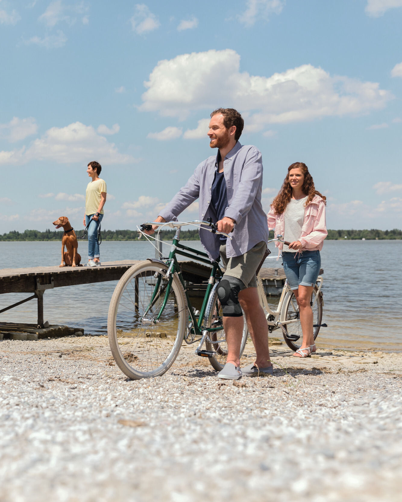 Homem com joelheira empurra a sua bicicleta junto ao lago