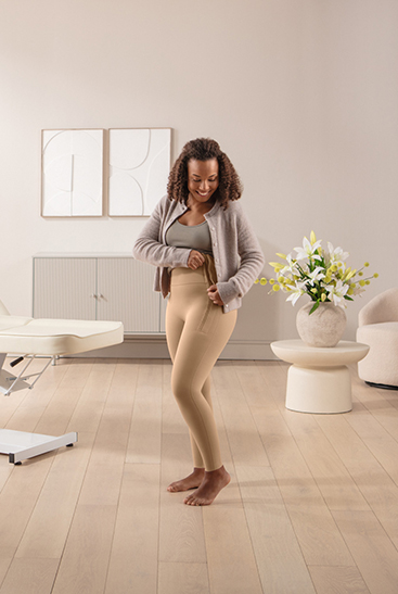 Eine dunkelhaarige Frau schließt gerade den Reißverschluss der Juzo Comprima Leggins