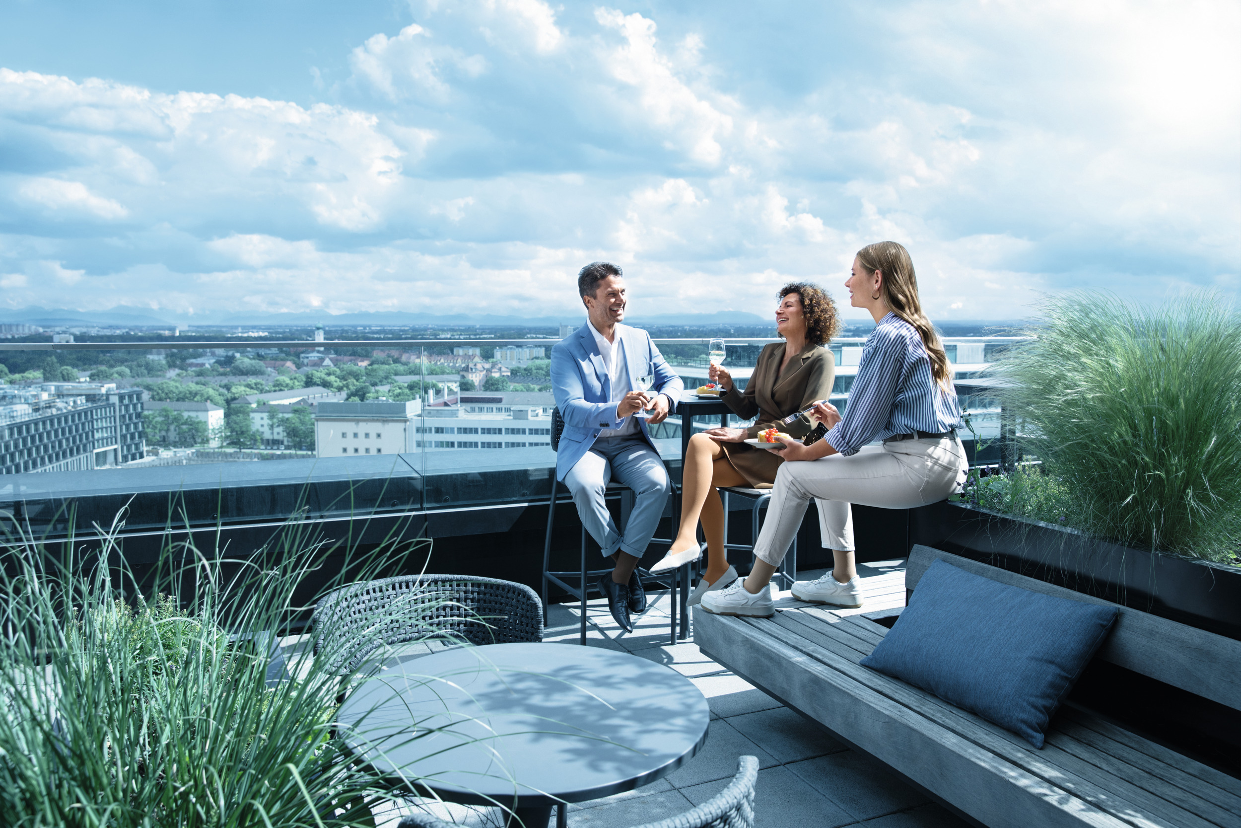 A man and two women are sitting on a roof terrace. They are chatting and are wearing compression stockings.