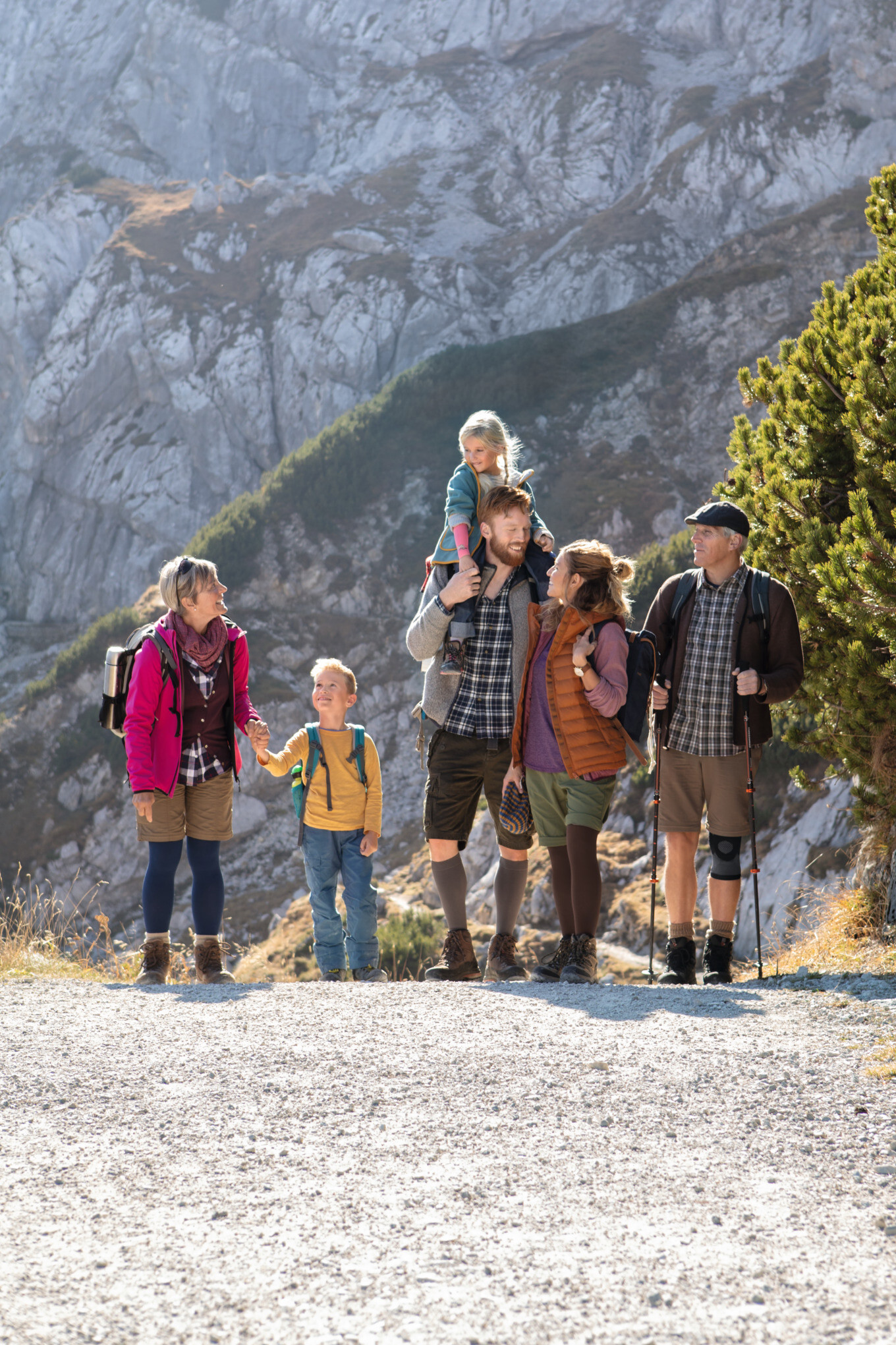 Gruppe von wandernden Personen mit Kindern auf einem sonnigen Bergweg; einige tragen Kompressionsstrümpfe und Bandagen Gruppe von wandernden Personen mit Kindern auf einem sonnigen Bergweg; einige tragen Kompressionsstrümpfe und Bandagen