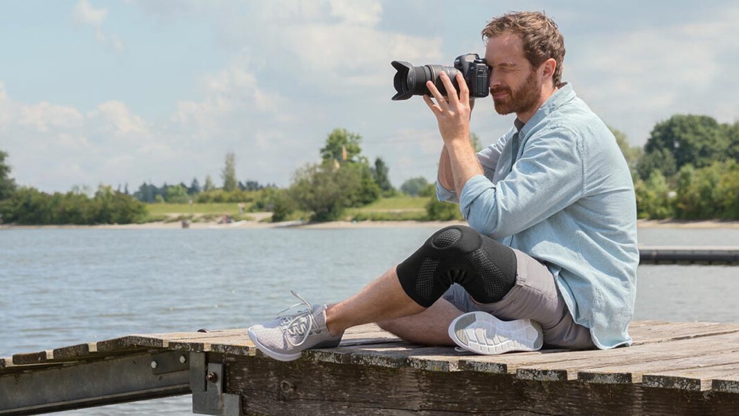 En fotograf sidder på en bro. Han har en Juzo-knæbandage på En fotograf sidder på en bro. Han har en Juzo-knæbandage på