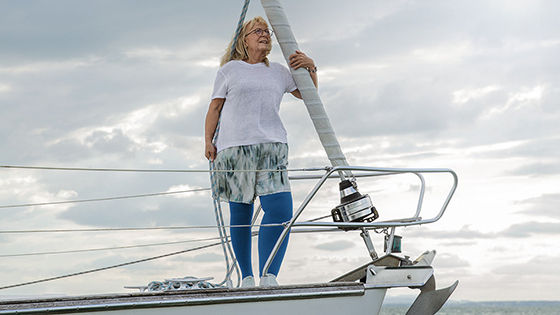 Frau mit einem Lymphödem steht auf dem Deck eines Bootes. Sie trägt blaue Kompressionsstrümpfe