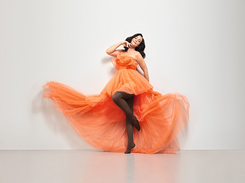 Mulher com um vestido laranja. Ela usa as meias-calças Juzo Inspiration na cor castanha. Mulher com um vestido laranja. Ela usa as meias-calças Juzo Inspiration na cor castanha.