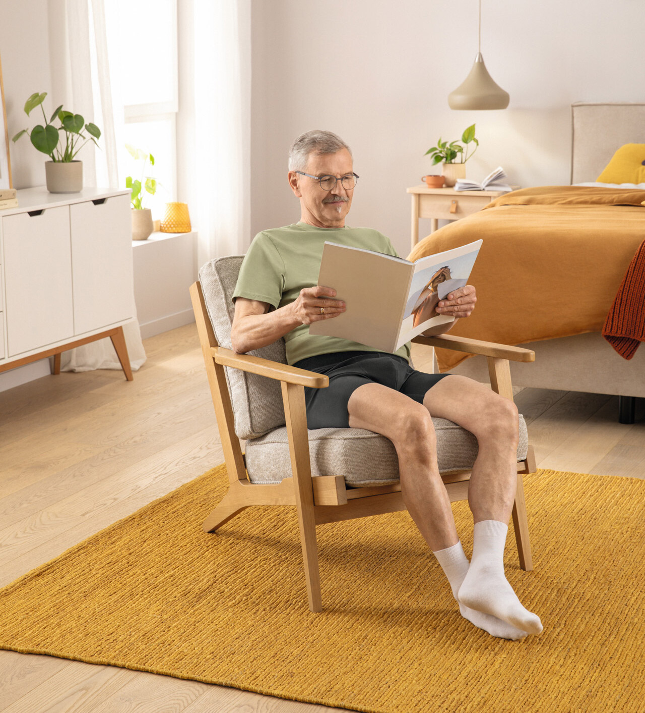 Ein Mann sitzt mit einer Zeitschrift auf einem Sessel und trägt die Juzo GenitalCompress Shorts Ein Mann sitzt mit einer Zeitschrift auf einem Sessel und trägt die Juzo GenitalCompress Shorts