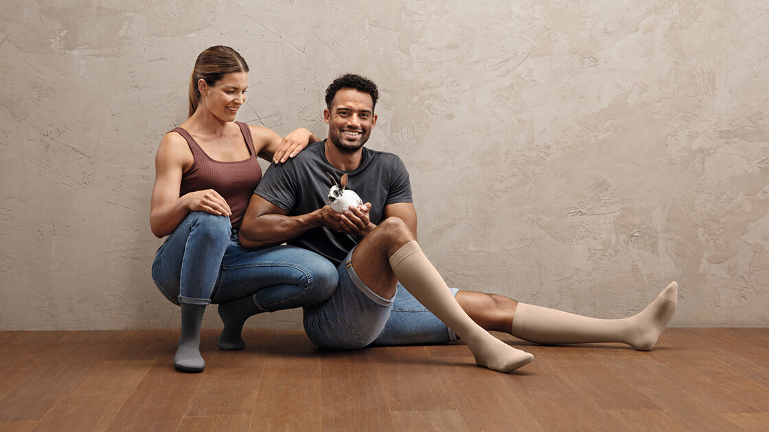 An athletic couple is sitting on the floor. Both are wearing Juzo Intenso compression stockings. The man is holding a bunny in his hand. An athletic couple is sitting on the floor. Both are wearing Juzo Intenso compression stockings. The man is holding a bunny in his hand.