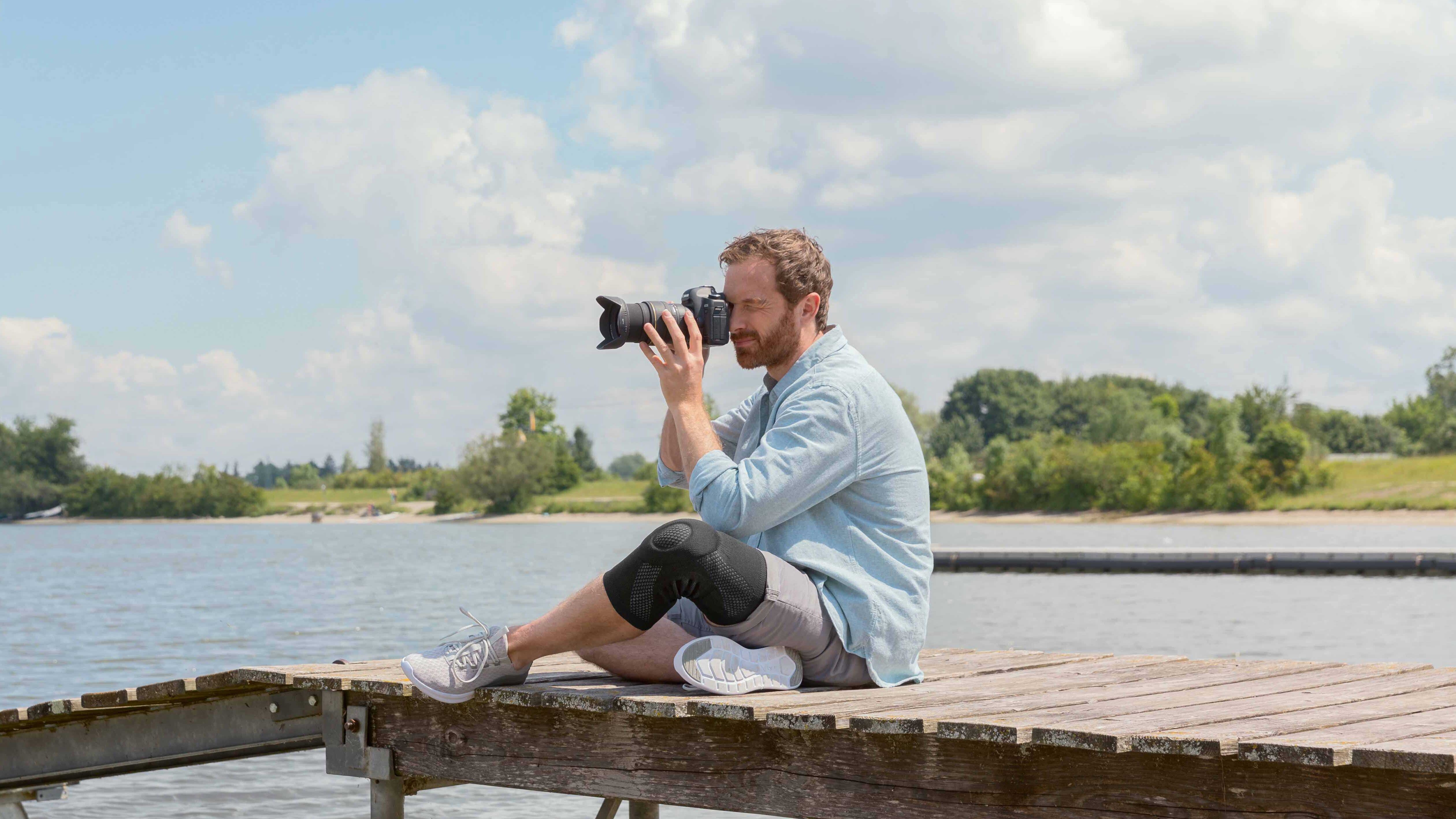 Un photographe est assis sur un ponton. Il porte une genouillère Juzo Un photographe est assis sur un ponton. Il porte une genouillère Juzo