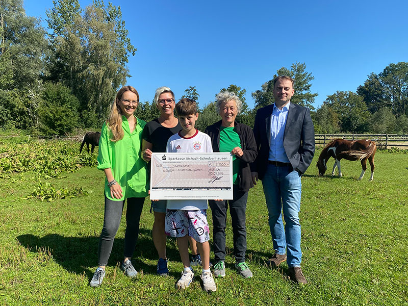 Auf dem Bild sieht man 2 Frauen, einen Mann und einen Jungen, der einen großen Scheck in der Hand hält