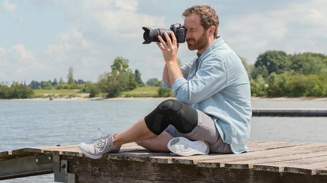 En fotograf sitter på en brygga. Han bär ett Juzo-knäbandage En fotograf sitter på en brygga. Han bär ett Juzo-knäbandage