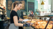 Bäckereiverkäuferin trägt Handgelenkbandage JuzoFlex Manu Xtra und greift mit einer Servierzange nach einem Croissant