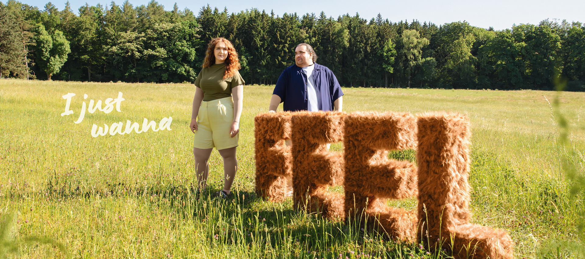 I just wanna Feel Ein Mann und eine Frau stehen auf einer Wiese neben den Buchstaben Feel