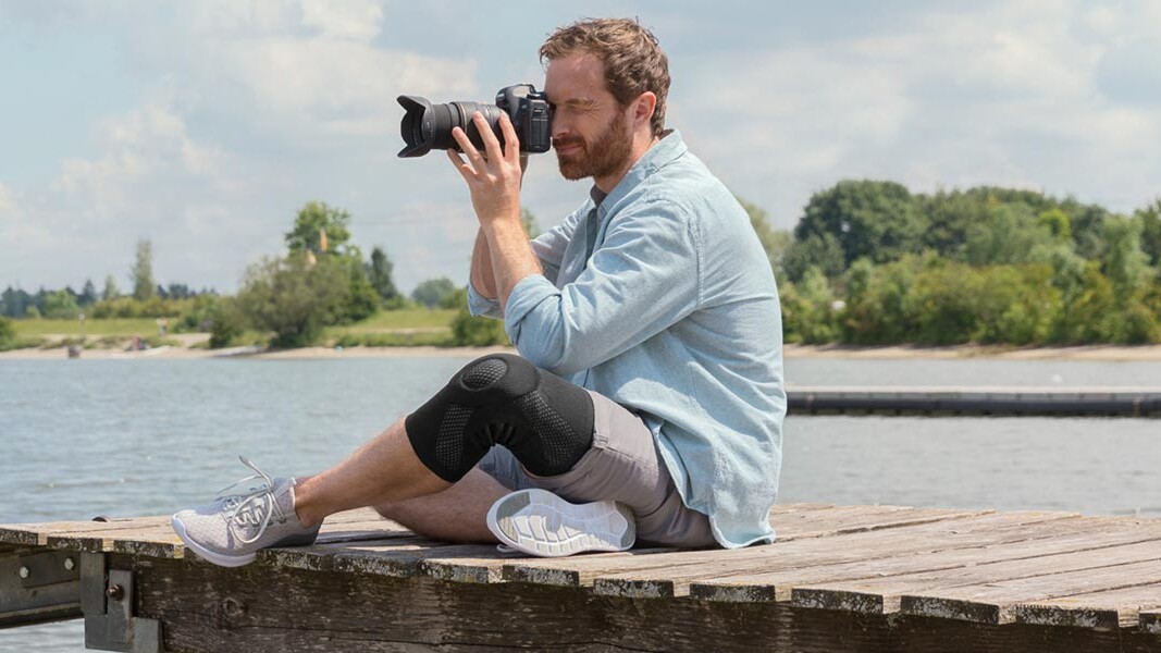 En fotograf sitter på en brygga. Han bär ett Juzo-knäbandage