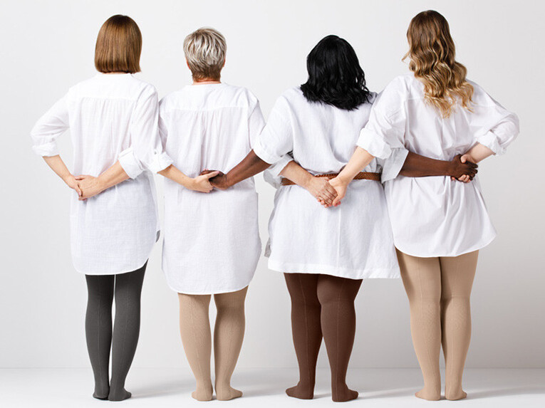 Vier Frauen stehen mit dem Rücken zum Betrachter und halten sich an den Händen