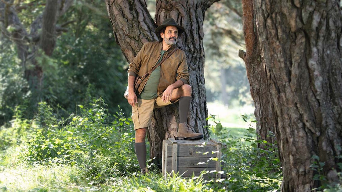 Un hombre vestido con ropa de explorador está en plena naturaleza y mira hacia el horizonte. Lleva medias de compresión que le llegan hasta las rodillas. Un hombre vestido con ropa de explorador está en plena naturaleza y mira hacia el horizonte. Lleva medias de compresión que le llegan hasta las rodillas.