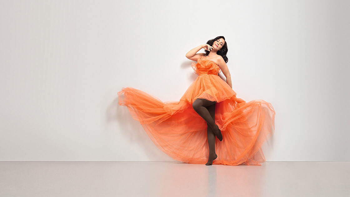 Une femme en robe orange. Elle porte les collants marron « Juzo Inspiration Une femme en robe orange. Elle porte les collants marron « Juzo Inspiration
