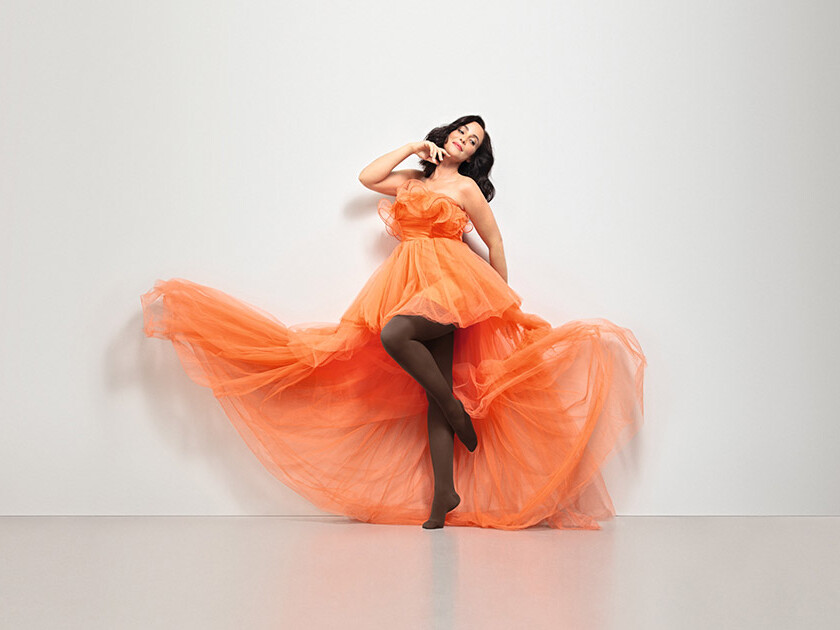 Mulher com um vestido laranja. Ela usa as meias-calças Juzo Inspiration na cor castanha. Mulher com um vestido laranja. Ela usa as meias-calças Juzo Inspiration na cor castanha.