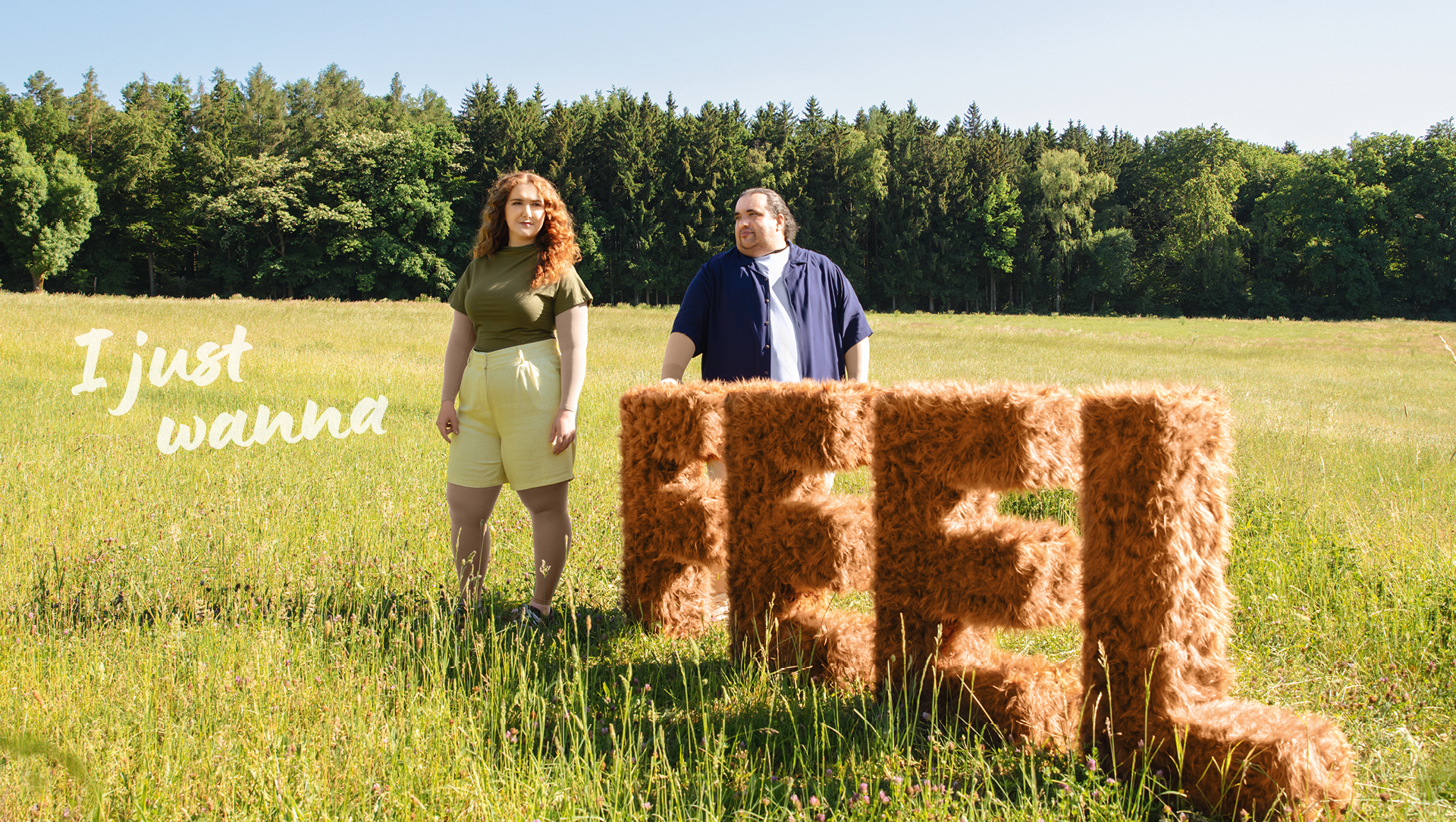 I just wanna Feel Ein Mann und eine Frau stehen auf einer Wiese neben den Buchstaben Feel