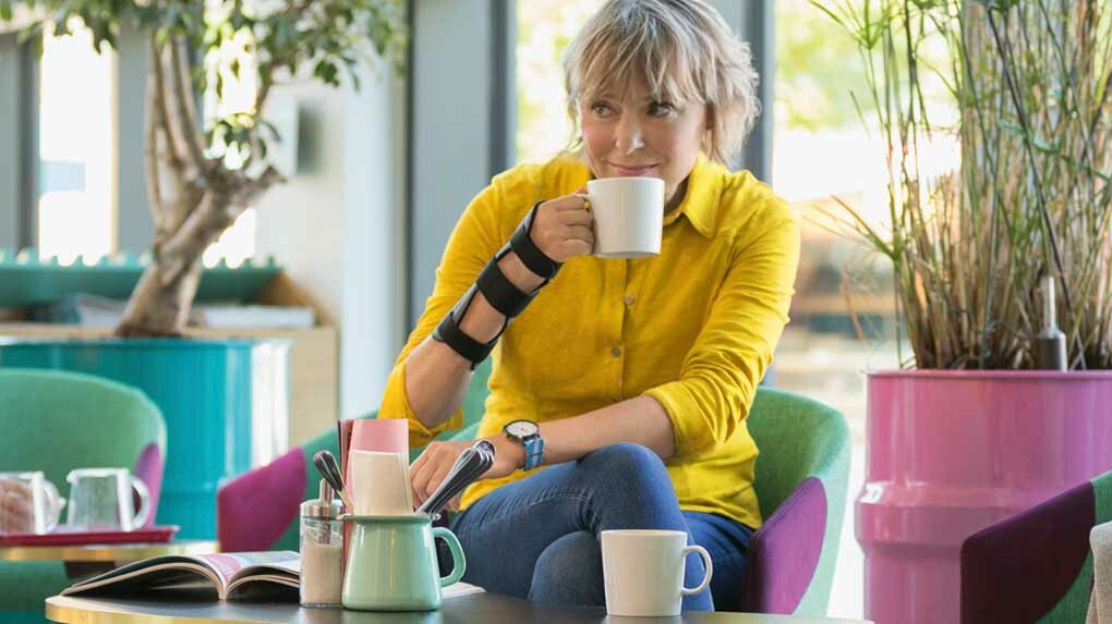 Carpal tunnel syndrome A woman sits in a café. She is drinking a coffee and wearing an orthosis on her wrist.