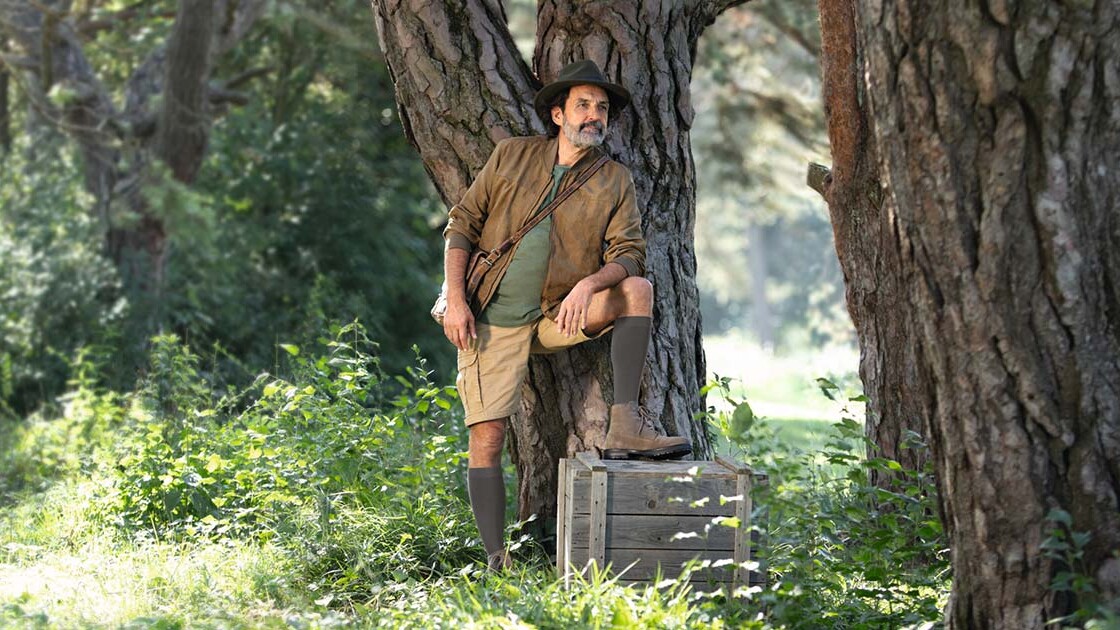 Un homme vêtu d'une tenue d'explorateur se tient en pleine nature et regarde au loin. Il porte des bas de contention qui lui arrivent aux genoux. Un homme vêtu d'une tenue d'explorateur se tient en pleine nature et regarde au loin. Il porte des bas de contention qui lui arrivent aux genoux.