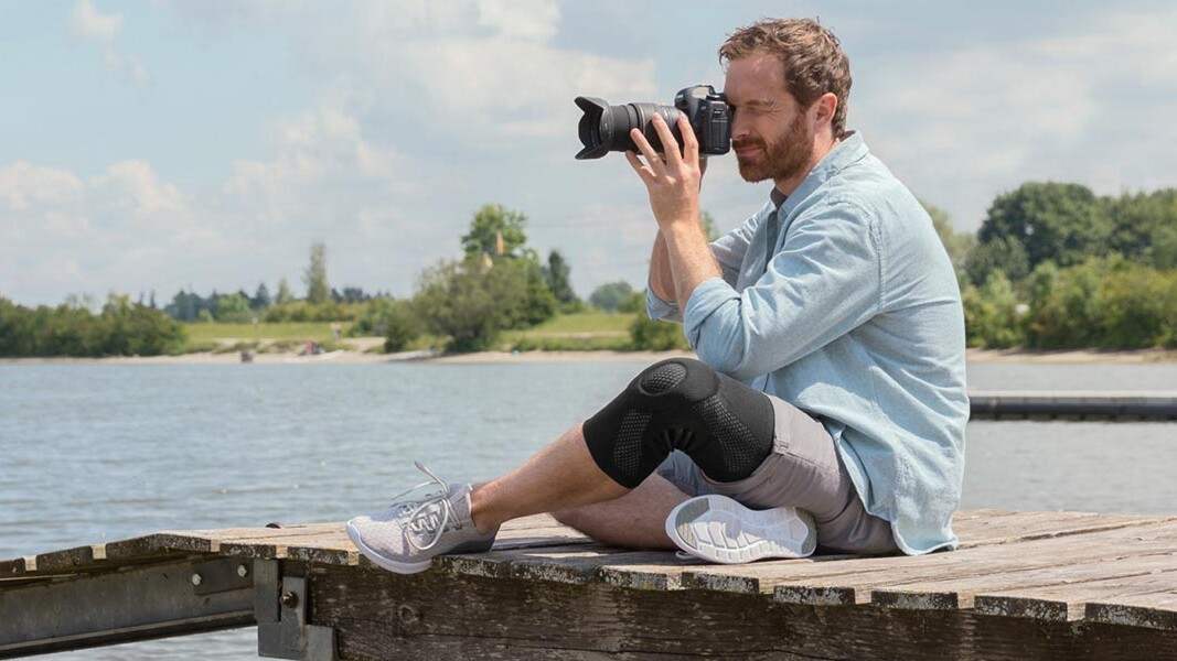 Un photographe est assis sur une passerelle. Il porte une genouillère Juzo. Un photographe est assis sur une passerelle. Il porte une genouillère Juzo.