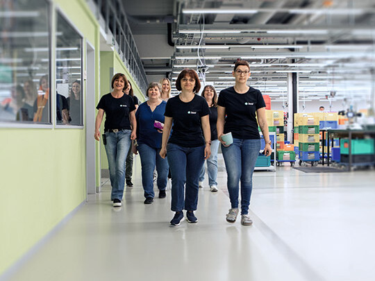 Sieben Frauen mit schwarzen Juzo T-Shirts laufen durch unsere Produktion