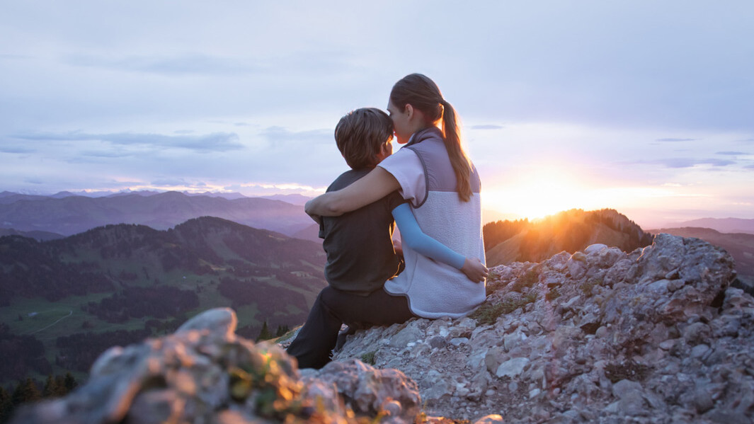 A mother is sitting on a mountain peak with her child. The child is wearing a compression sleeve.