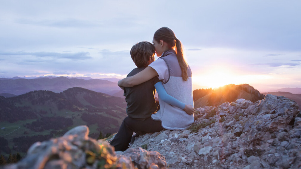 Una madre está sentada con su hijo en la cima de una montaña. El niño lleva una manga de compresión. Una madre está sentada con su hijo en la cima de una montaña. El niño lleva una manga de compresión.