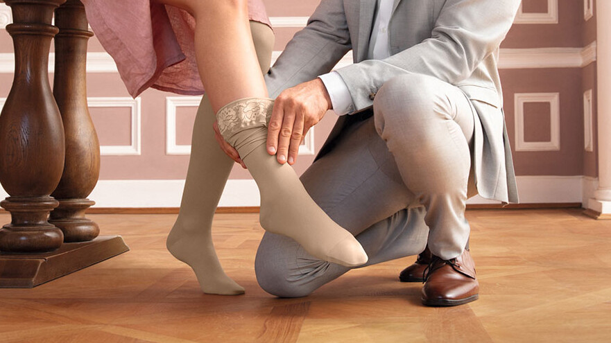 Un hombre le pone una media de compresión a una mujer. El escenario tiene un aire de cuento de hadas, como en «La Cenicienta». Un hombre le pone una media de compresión a una mujer. El escenario tiene un aire de cuento de hadas, como en «La Cenicienta».