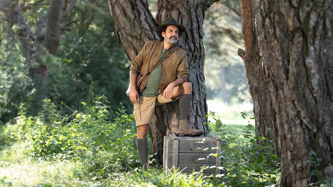 Un homme vêtu d'une tenue d'explorateur se tient en pleine nature et regarde au loin. Il porte des bas de contention qui lui arrivent aux genoux. Un homme vêtu d'une tenue d'explorateur se tient en pleine nature et regarde au loin. Il porte des bas de contention qui lui arrivent aux genoux.