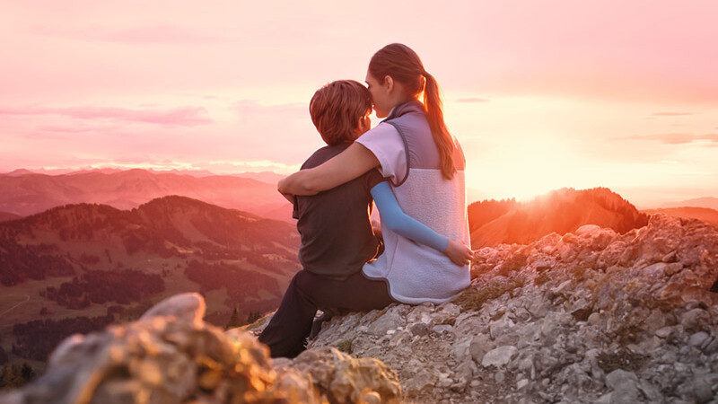 Eine Mutter sitzt mit ihrem Kind auf einem Berggipfel. Das Kind trägt einen Kompressionsärmel.