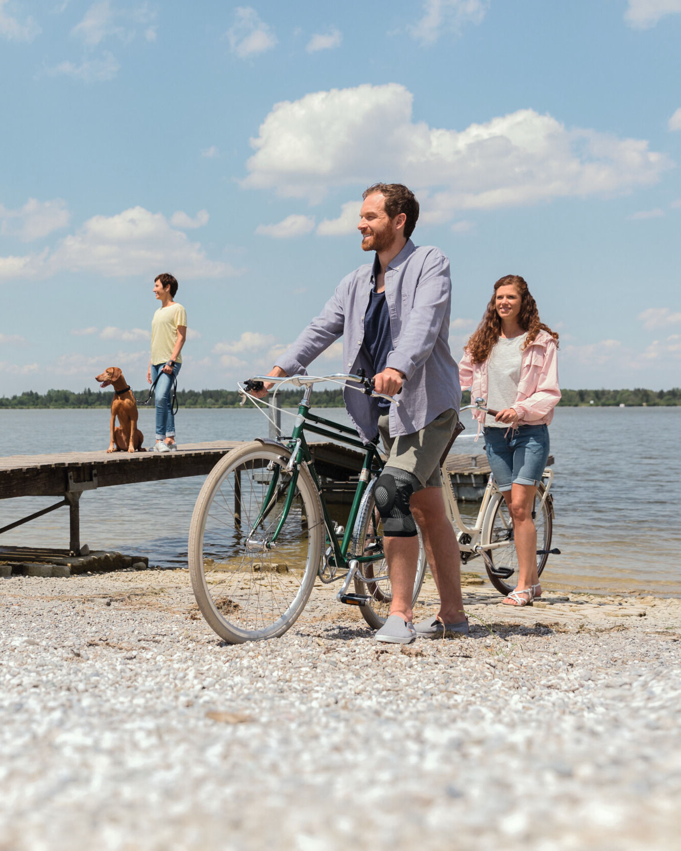 Een man met een kniebrace duwt zijn fiets langs het meer Een man met een kniebrace duwt zijn fiets langs het meer