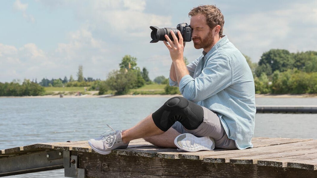 En fotograf sidder på en bro. Han har en Juzo-knæbandage på En fotograf sidder på en bro. Han har en Juzo-knæbandage på