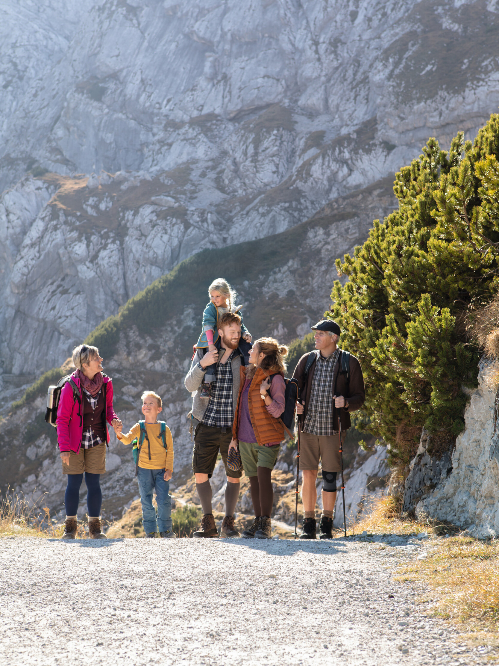 Groupe de randonneurs accompagnés d'enfants sur un sentier de montagne ensoleillé ; certains portent des bas de contention et des bandages Groupe de randonneurs accompagnés d'enfants sur un sentier de montagne ensoleillé ; certains portent des bas de contention et des bandages