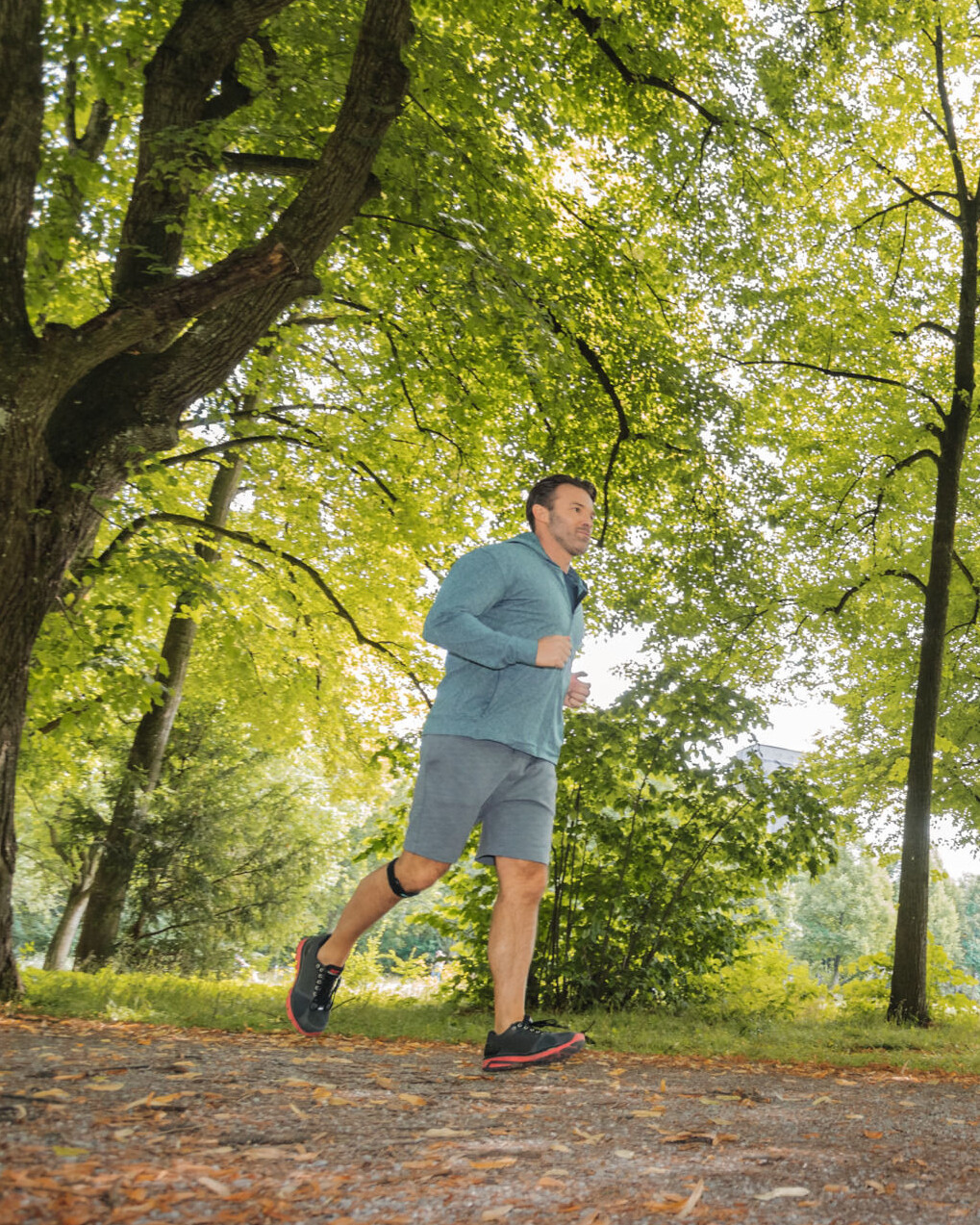 Ein Mann joggt im Wald. Er trägt ein Patellasehnenband Ein Mann joggt im Wald. Er trägt ein Patellasehnenband