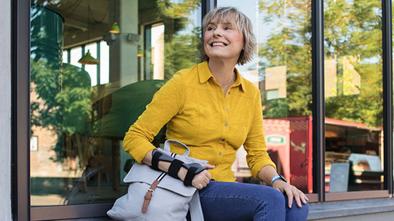 Ortoser A woman sits on a windowsill. She is wearing a wrist orthosis on her wrist.