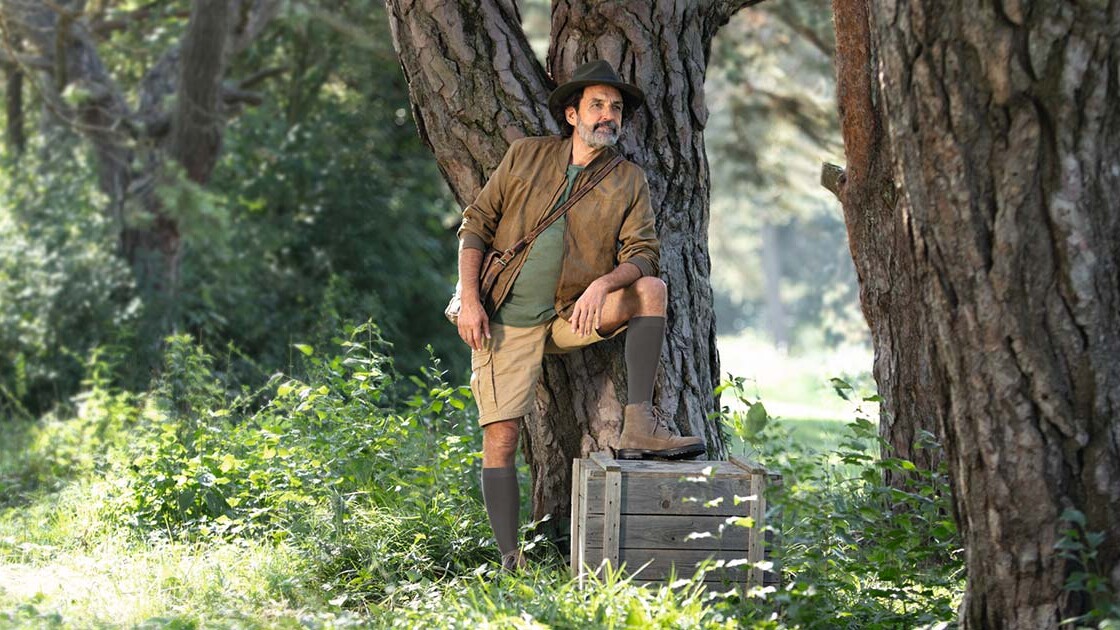 Un homme vêtu d'une tenue d'explorateur se tient en pleine nature et regarde au loin. Il porte des bas de contention qui lui arrivent aux genoux. Un homme vêtu d'une tenue d'explorateur se tient en pleine nature et regarde au loin. Il porte des bas de contention qui lui arrivent aux genoux.