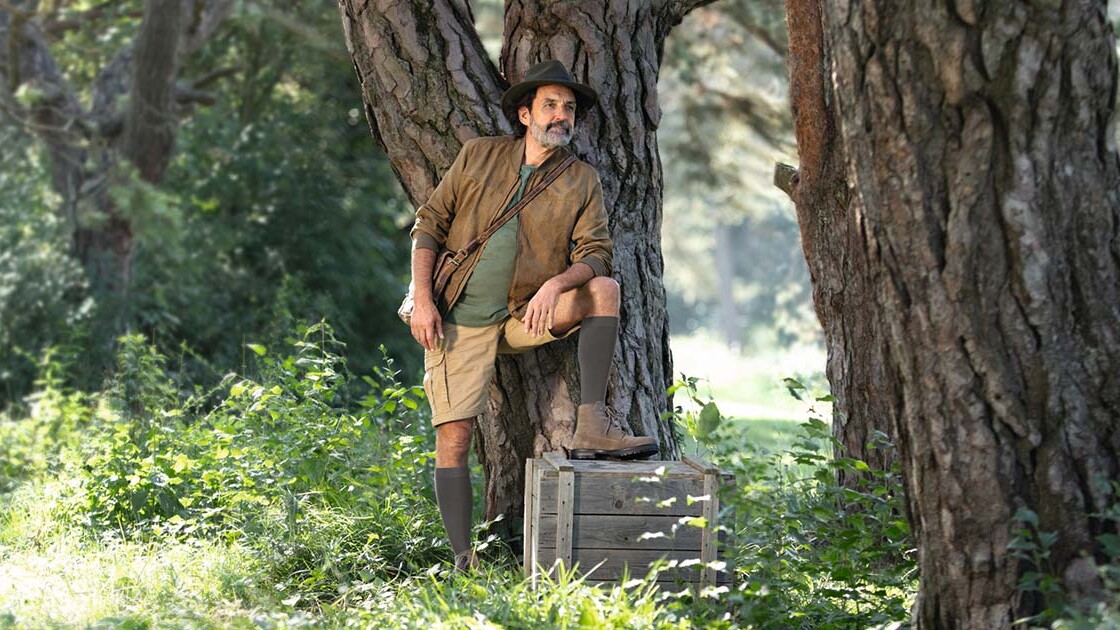 A man dressed in explorer gear is standing in the great outdoors, gazing into the distance. He is wearing knee-high compression socks. A man dressed in explorer gear is standing in the great outdoors, gazing into the distance. He is wearing knee-high compression socks.