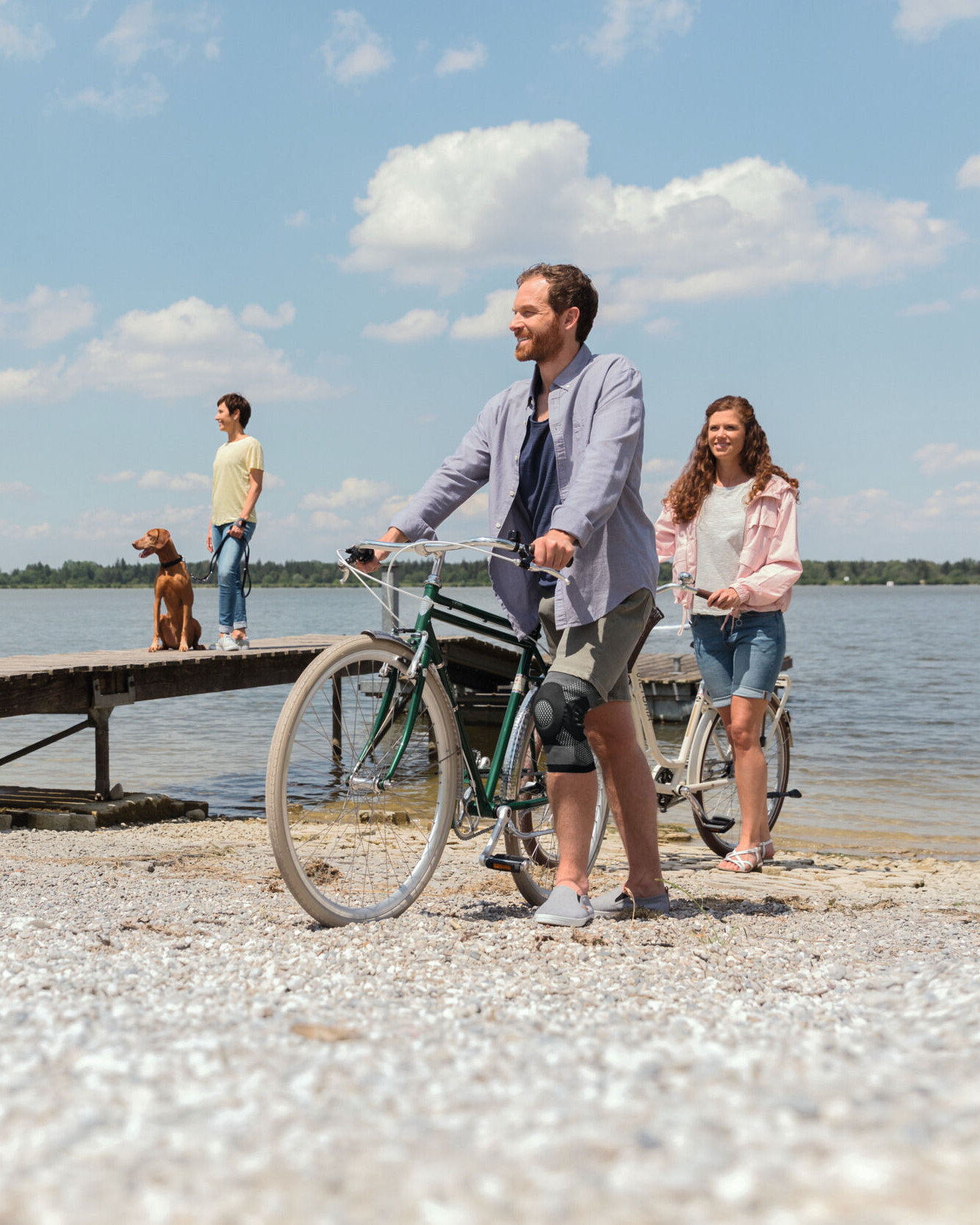 Un hombre con una rodillera empuja su bicicleta junto al lago