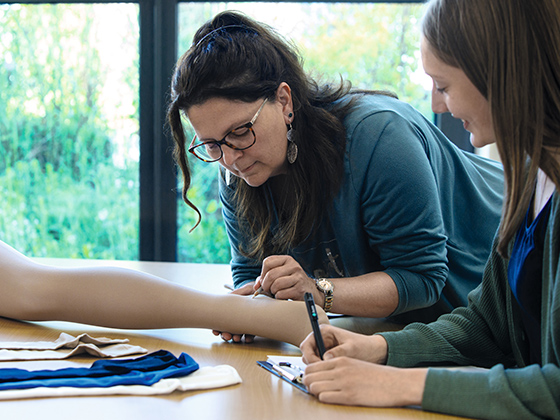 Zwei Mitarbeiterinnen überprüfen eine Strumpf an einem Dekobein