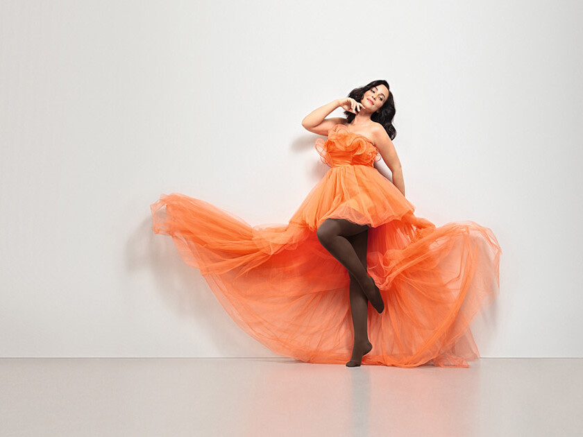 Frau in orangenem Kleid. Sie trägt den Juzo Inspiration als braune Strumpfhose Frau in orangenem Kleid. Sie trägt den Juzo Inspiration als braune Strumpfhose