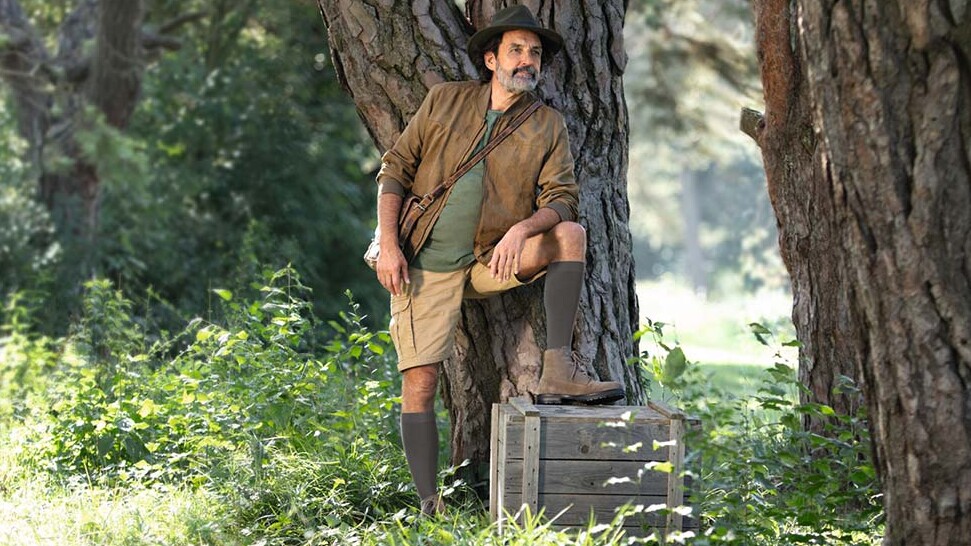 A man dressed in explorer gear is standing in the great outdoors, gazing into the distance. He is wearing knee-high compression socks. A man dressed in explorer gear is standing in the great outdoors, gazing into the distance. He is wearing knee-high compression socks.