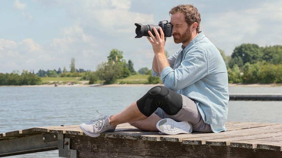 A photographer is sitting on a dock. He is wearing a Juzo knee support. A photographer is sitting on a dock. He is wearing a Juzo knee support.