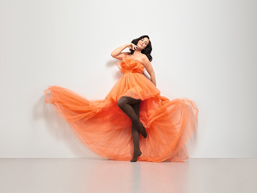 A woman in an orange dress. She is wearing Juzo Inspiration brown tights.