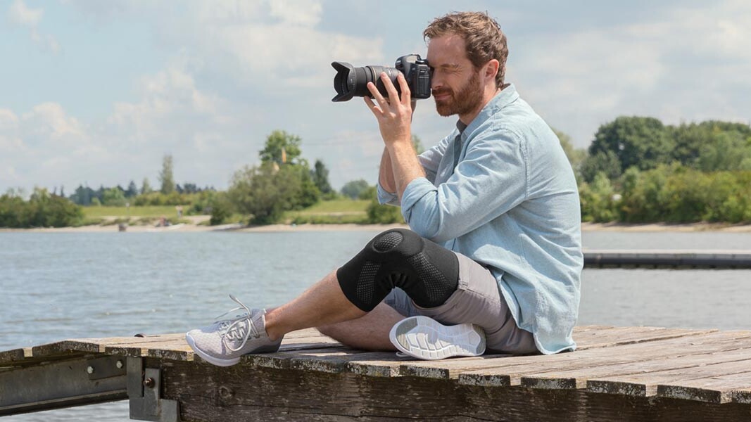 Een fotograaf zit op een steiger. Hij draagt een Juzo-kniebandage