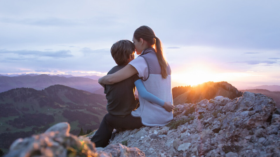 En mamma sitter med sitt barn på en bergstopp. Barnet bär en kompressionsärm. En mamma sitter med sitt barn på en bergstopp. Barnet bär en kompressionsärm.