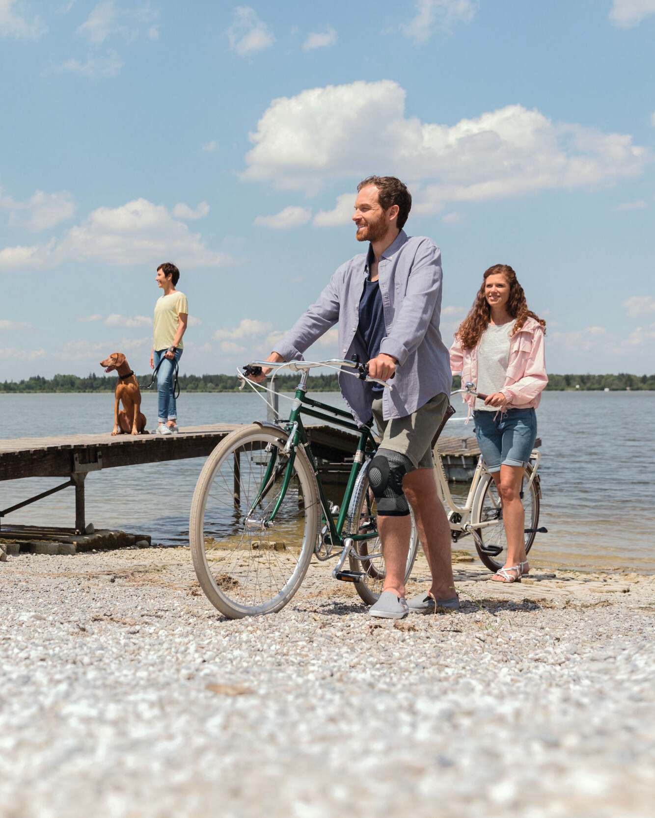 Een man met een kniebandage duwt zijn fiets langs het meer