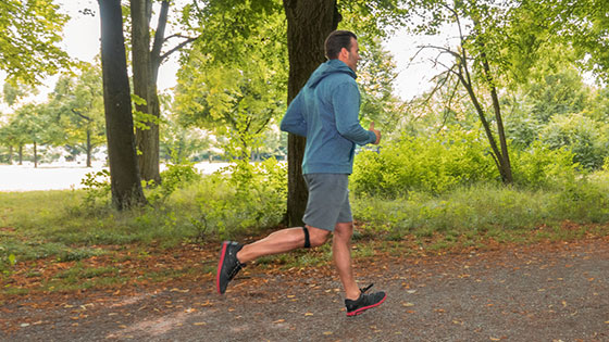 Patella tip syndrome A man jogging in the forest wearing a JuzoFlex Patella Xtra